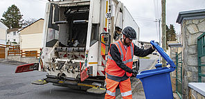 Un agent réalise la collecte d'un bac bleu de déchets recyclables