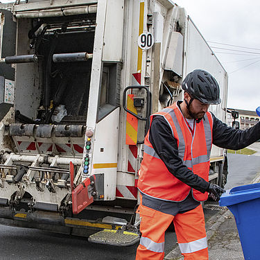 Un agent réalise la collecte d'un bac bleu de déchets recyclables