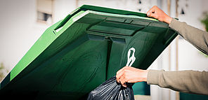 personne mettant un sac poubelle dans un grand bac vert Limoges Métropole