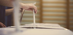 Une personne tient son bulletin de vote et s'apprête à le mettre dans une urne.