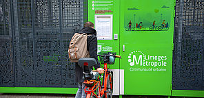 Une personne avec un vélo est en train de lire le règlement d'une consigne de stationnement vélos autonome en énergie.